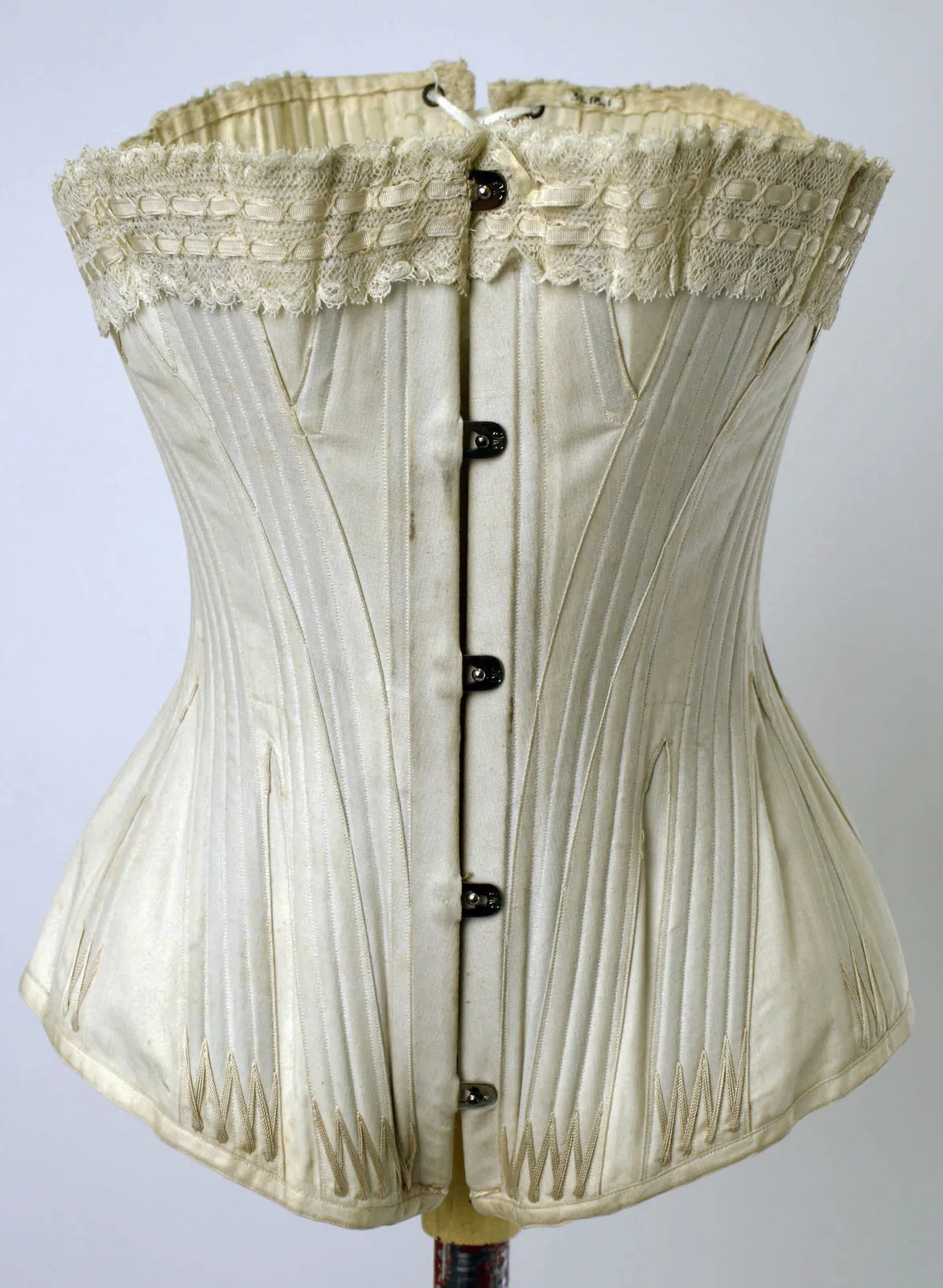 Cream corset with lace at the top and five metal studs and loops closing the front; American, 1880s; The Met C.I.39.18.1